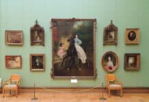 Картина в рамке, много портретов и пейзажей, покоящиеся на зеленой стене в музее, классическая живопись.